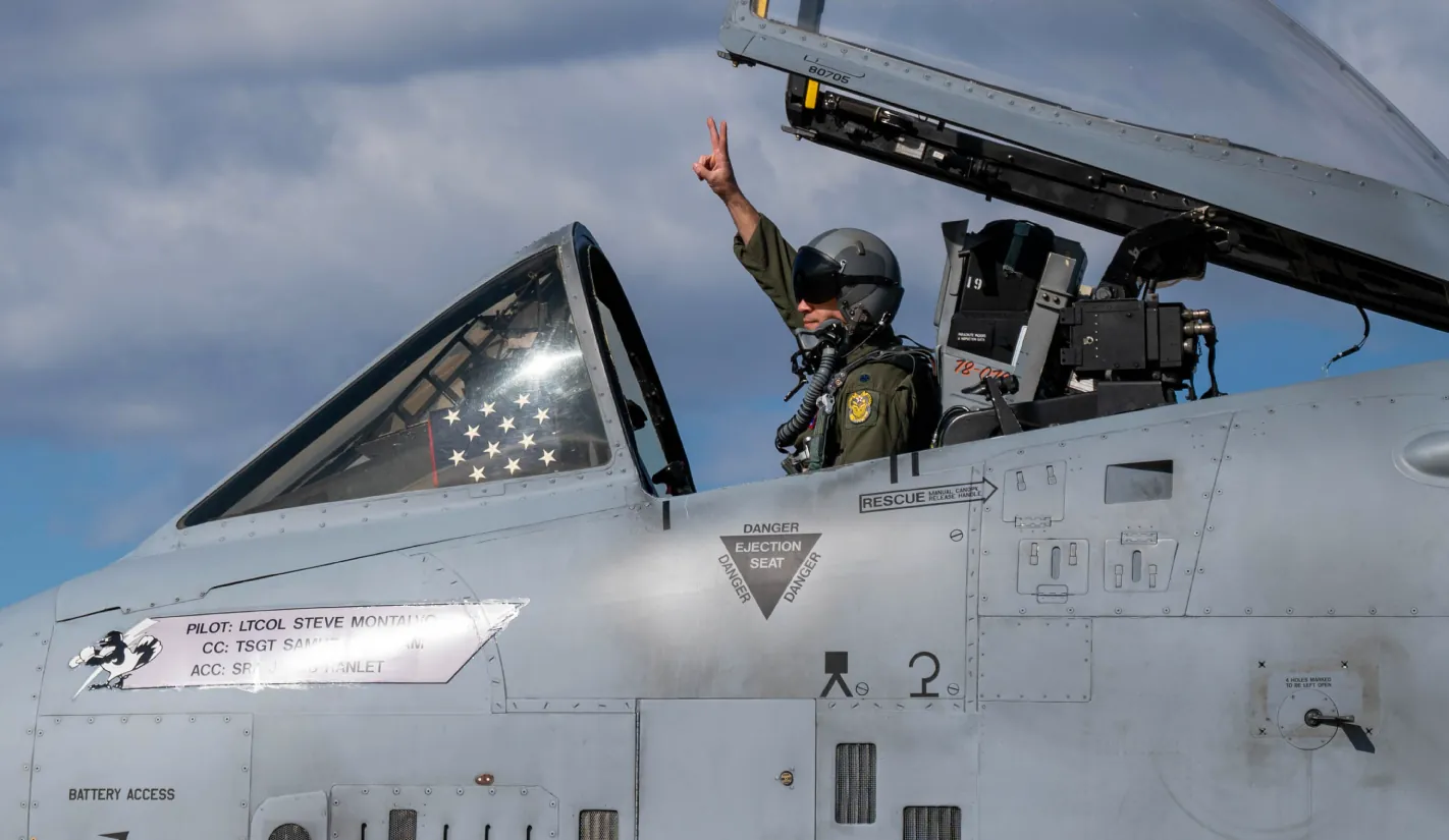 Military pilot inside aircraft cockpit raising hand in gesture – defense aviation readiness and operations