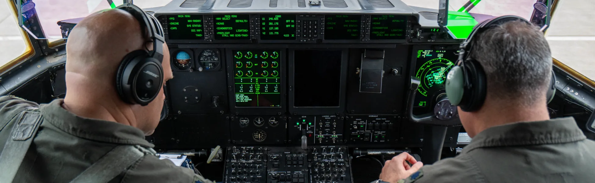 Two pilots operating the cockpit of a military transport aircraft with illuminated control panels